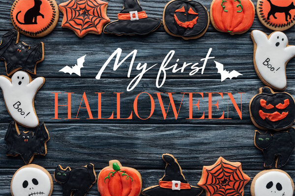 frame made of spooky halloween homemade cookies on black wooden background with bats "my first halloween" lettering 