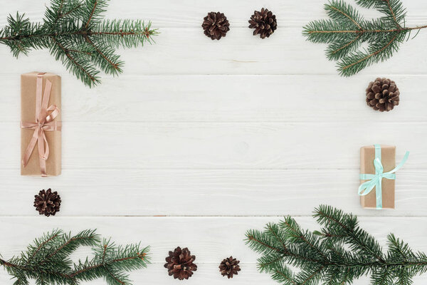 top view of evergreen coniferous branches, pine cones and christmas presents on white wooden background