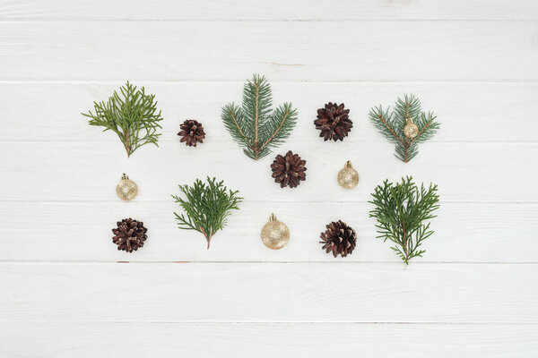 top view of shiny golden baubles, pine cones and evergreen coniferous branches on wooden surface