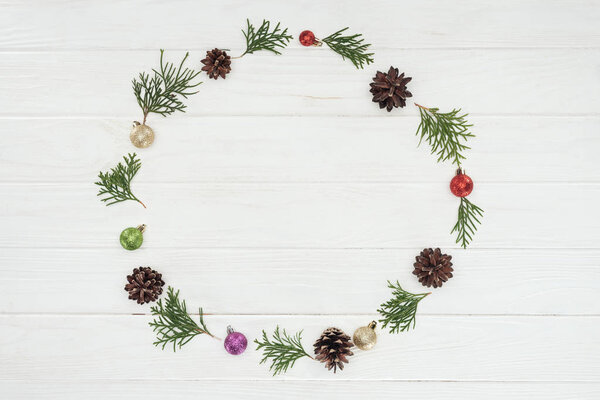top view of evergreen coniferous twigs, pine cones and baubles on wooden background 