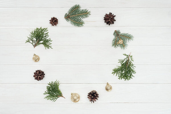 top view of evergreen coniferous twigs, pine cones and golden baubles on wooden background 