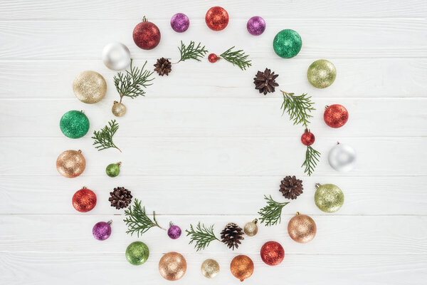 top view of beautiful shiny colorful baubles, coniferous twigs and pine cones on wooden surface, christmas background 