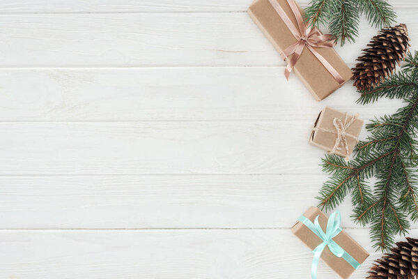 top view of christmas presents, fir twigs and pine cones on wooden background