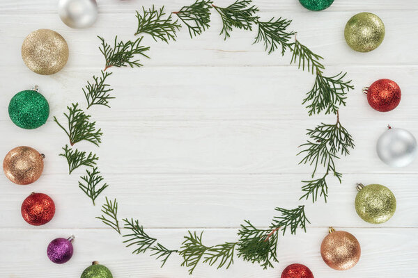 top view of round frame of coniferous twigs and shiny colorful baubles on wooden background