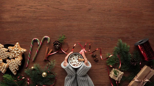 在木质背景下用可可和棉花糖 糖果手杖和圣诞装饰品的人拿着杯子的裁剪镜头 — 图库照片