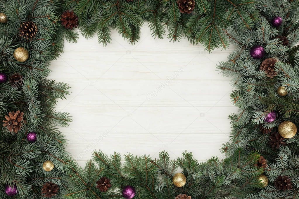 top view of beautiful evergreen fir twigs with shiny baubles and pine cones on white wooden background  