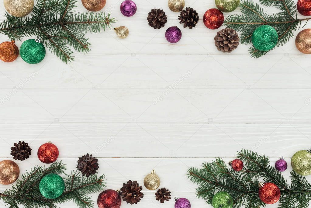 top view of colorful shiny christmas balls, fir twigs and pine cones on white wooden background
