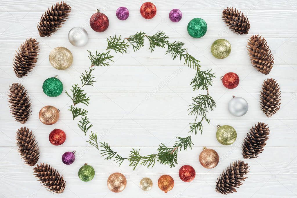 evergreen coniferous twigs, pine cones and shiny colorful baubles on white wooden background