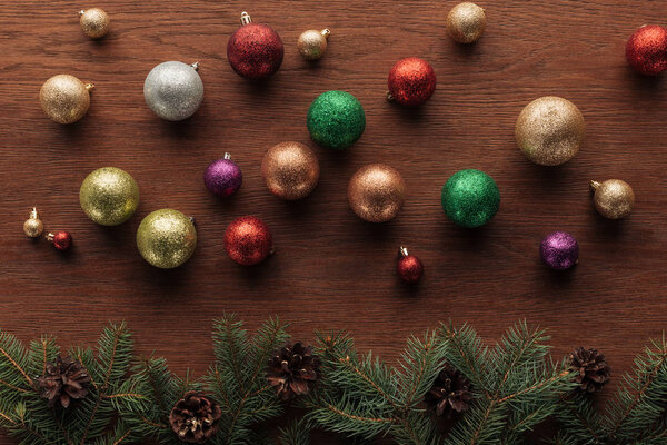 shiny colorful balls and coniferous twigs with pine cones on wooden background 