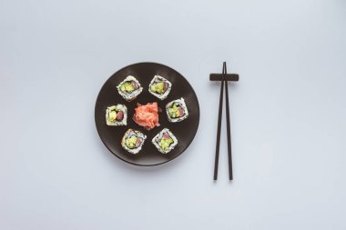 top view of delicious sushi with ginger on round plate and chopsticks isolated on white  clipart