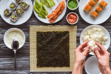 partial top view of person preparing rice for delicious sushi above wooden table clipart