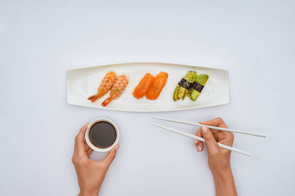 cropped shot of person holding chopsticks and bowl with soy sauce while eating sushi isolated on white