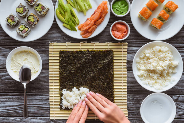 partial top view of person preparing sushi with rice, nori and ingredients
