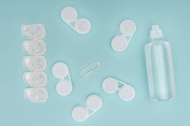 flat lay with sterile liquid in bottle, tweezers and containers for contact lenses storage on blue tabletop clipart