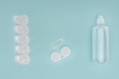 düz lay ile steril sıvı şişe, cımbız ve kontakt lens mavi masa üzerinde konteynerler