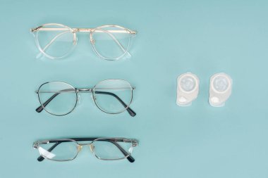 top view of eyeglasses and contact lenses containers arranged on blue background clipart
