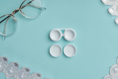 top view of eyeglasses and arranged contact lenses containers on blue background clipart