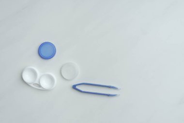 top view of contact lenses container and tweezers on white backdrop clipart