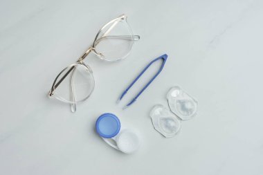 düz lay gözlük, kontakt lens kapsayıcılar ve beyaz yüzey üzerinde düzenlenmiş cımbız ile