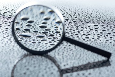 close up view of magnifying glass and water drops on grey backdrop  clipart
