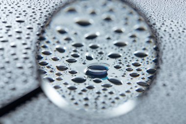 selective focus of magnifying glass and contact lense on grey background with water drops clipart