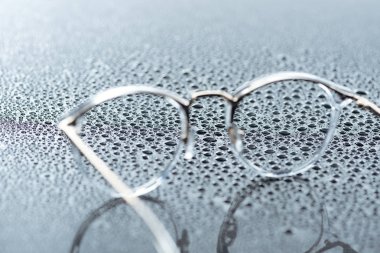 close up view of eyeglasses and water drops on grey backdrop clipart
