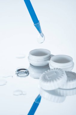 close up view of container, contact lenses and tweezers on white backdrop with reflection clipart