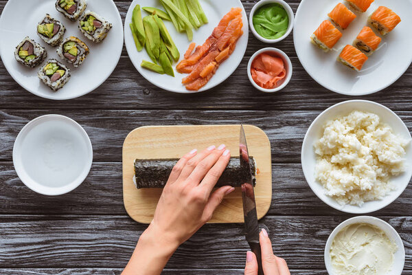 cropped shot of person holding knife and cutting delicious sushi roll