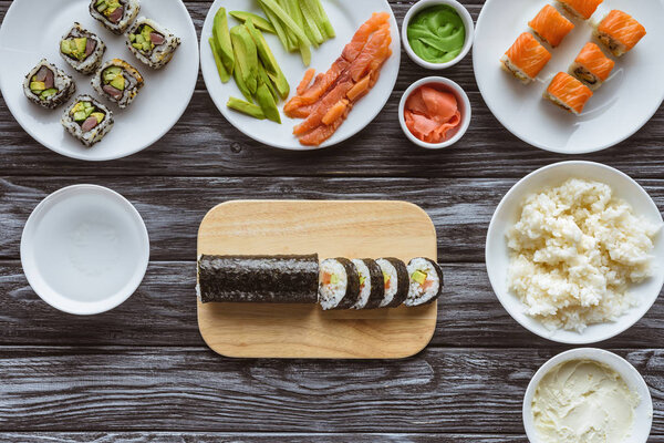 top view of delicious sushi rolls and ingredients on wooden table