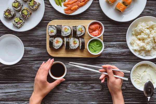 cropped shot of person holding chopsticks and eating delicious sushi