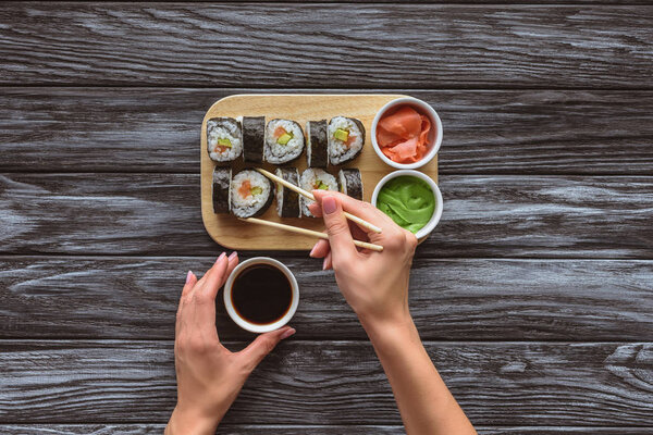 partial top view of person holding chopsticks and bowl with soy sauce while eating sushi 