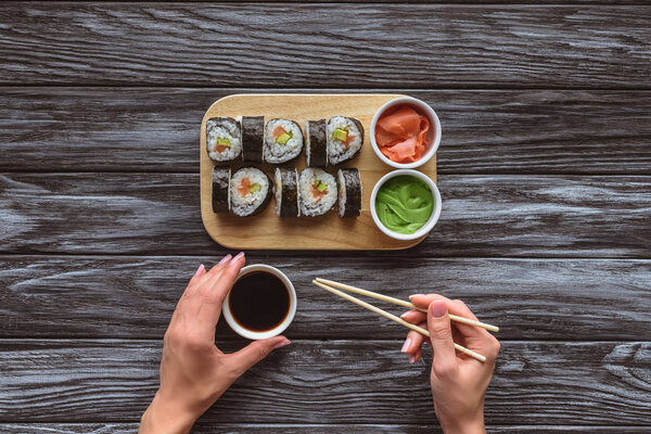 cropped shot of person holding chopsticks and bowl with soy sauce while eating sushi 