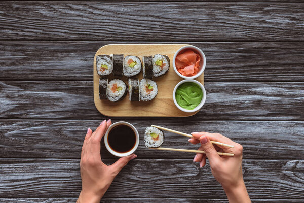 cropped shot of person holding chopsticks and eating delicious sushi roll 