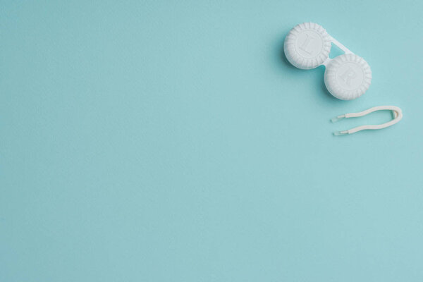 вид сверху на контейнер с белыми контактными линзами и пинцет на синем фоне
