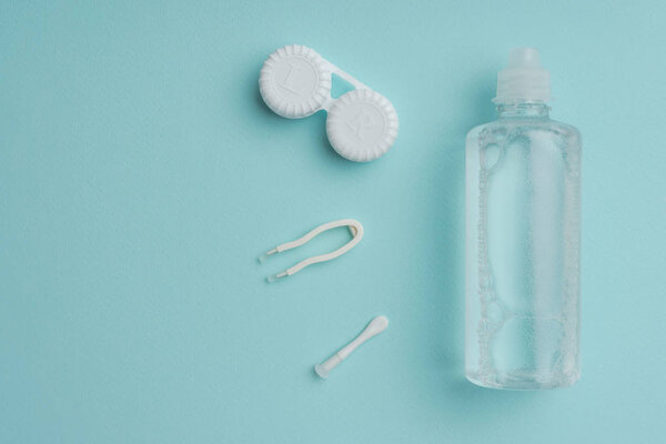 вид сверху на стерильную жидкость в бутылке, пинцете и контейнере для контактных линз на голубом столе
