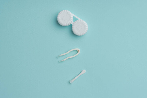 вид сверху на контейнер с белыми контактными линзами и пинцет на синем фоне
