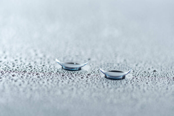 close up view of contact lenses on background with water drops