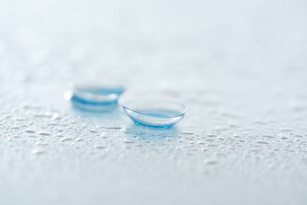 close up view of contact lenses on white background with water drops