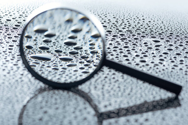 close up view of magnifying glass and water drops on grey backdrop 