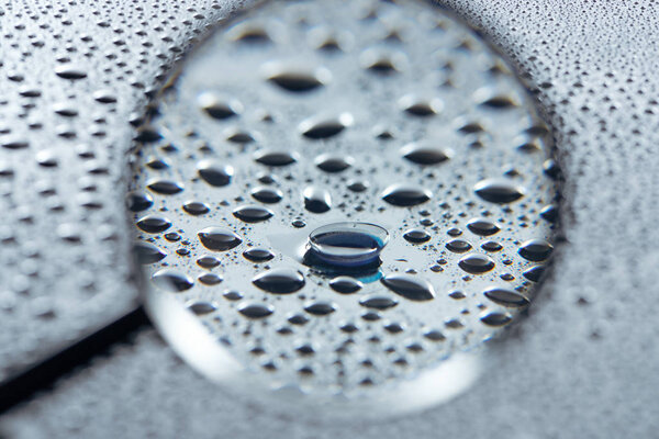 selective focus of magnifying glass and contact lense on grey background with water drops