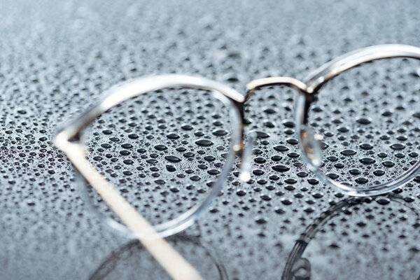 close up view of eyeglasses and water drops on grey backdrop