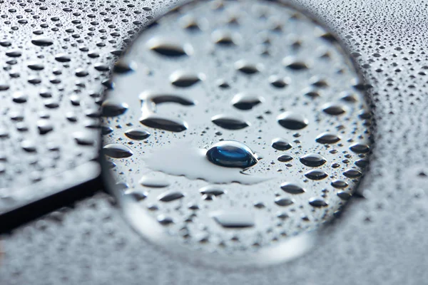 selective focus of magnifying glass and contact lense on grey background with water drops