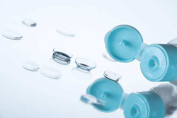 close up view of contact eye lenses and bottle with cleansing liquid on background with reflection