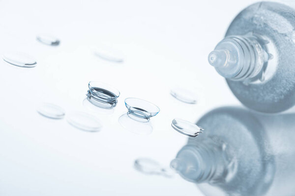 close up view of contact eye lenses and bottle with cleansing liquid on background with reflection
