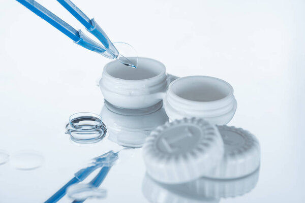 close up view of container for contact lenses and tweezers on white backdrop