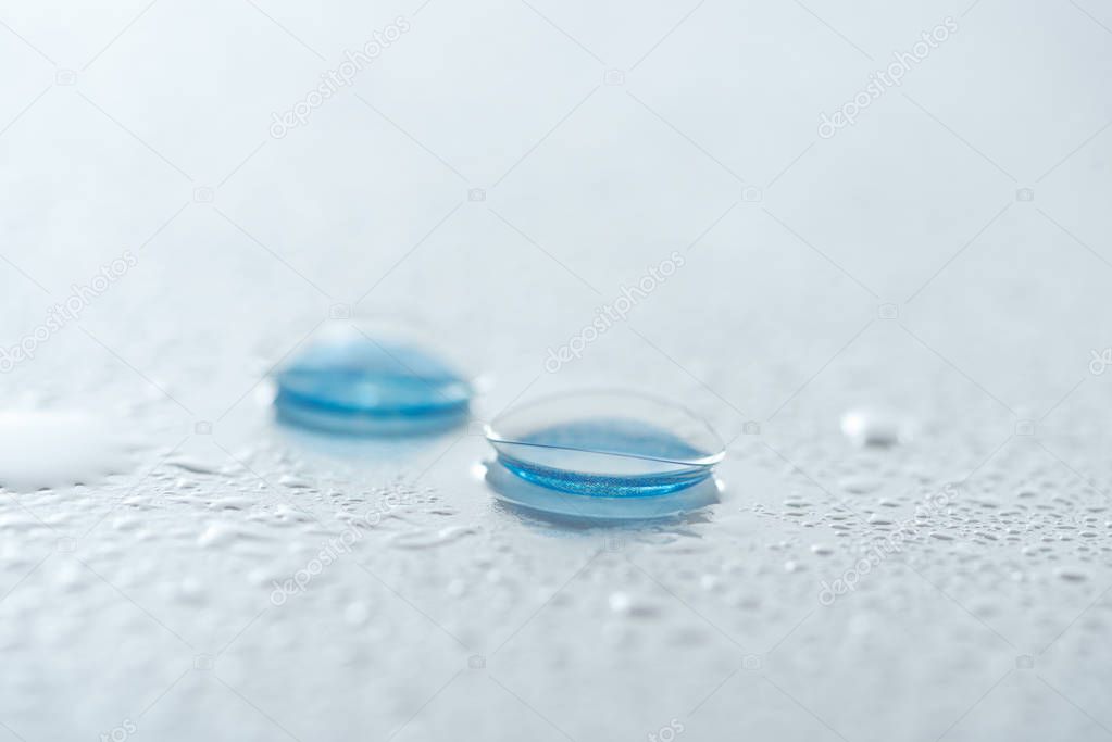 close up view of contact lenses on white background with water drops