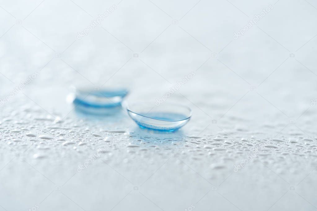 close up view of contact lenses on white background with water drops