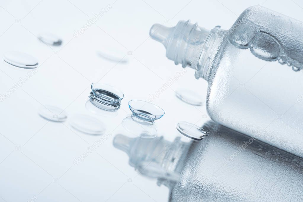 close up view of contact eye lenses and bottle with cleansing liquid on background with reflection