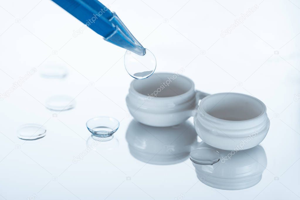 close up view of container for contact lenses and tweezers on white backdrop