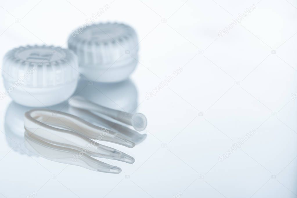 close up view of container for contact lenses and tweezers on background with reflection